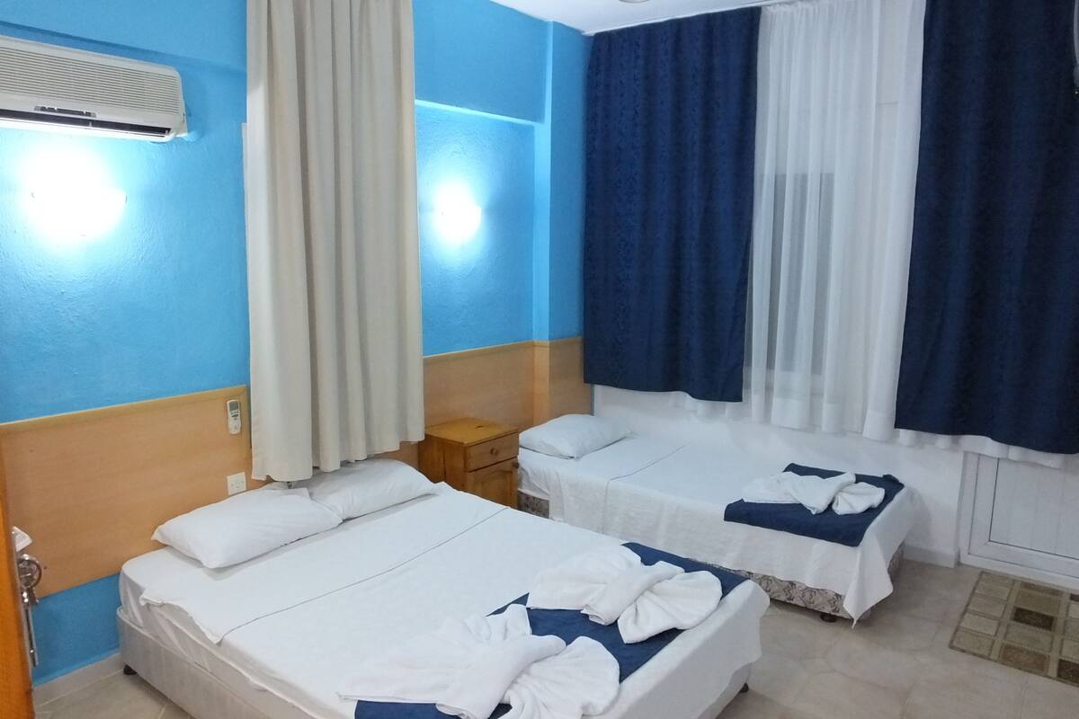 Une chambre d’hôtel avec deux lits, une table de chevet, une commode et une fenêtre avec des rideaux.