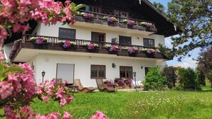 Un edificio de dos plantas con balcones, fachada blanca y un jardín delantero.