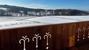 Un balcón de madera con vistas a un campo cubierto de nieve y árboles distantes.
