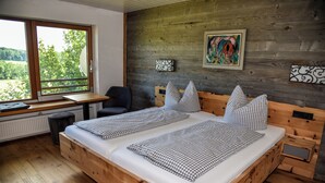 Una cama de madera con ropa de cama a cuadros, un escritorio con una silla, y una ventana con vistas a zonas verdes.