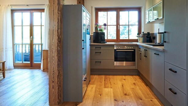 Una cocina moderna con suelo de madera, horno empotrado y un ventanal grande.