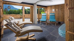 Ett spa-rum med träväggar, ett stort fönster och utsikt över en skog. Det finns tre fåtöljer och en blå stol.