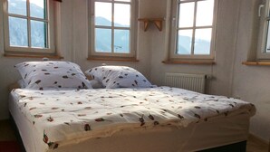 Een slaapkamer met een bed, twee ramen en uitzicht op bergen.