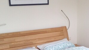 Une chambre à coucher avec une tête de lit en bois, deux jeux de draps à motifs et un tableau encadré accroché au mur.