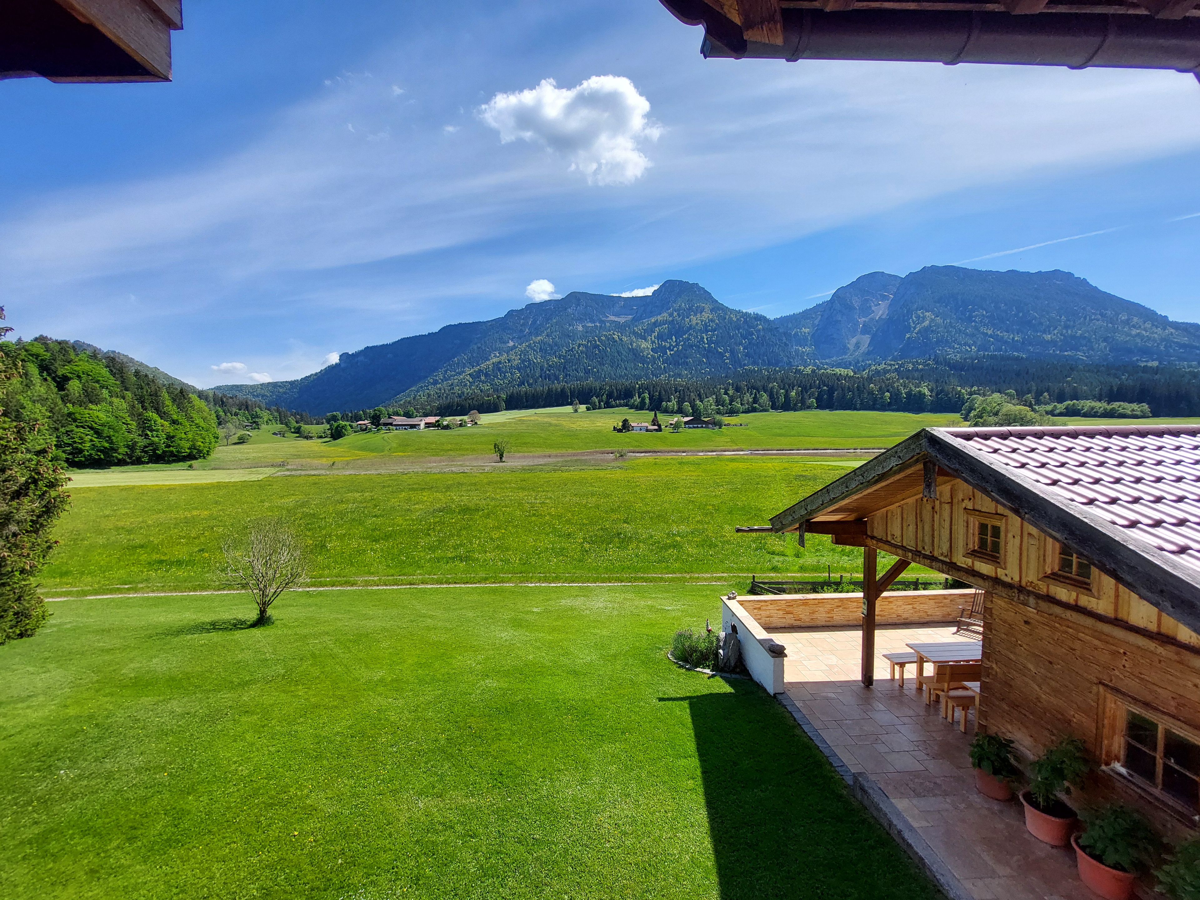 A wooden cabin with a patio, surrounded by green fields and mountains.