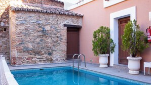 Una piscina amb parets de pedra i portes de fusta, envoltada de plantes en testos.