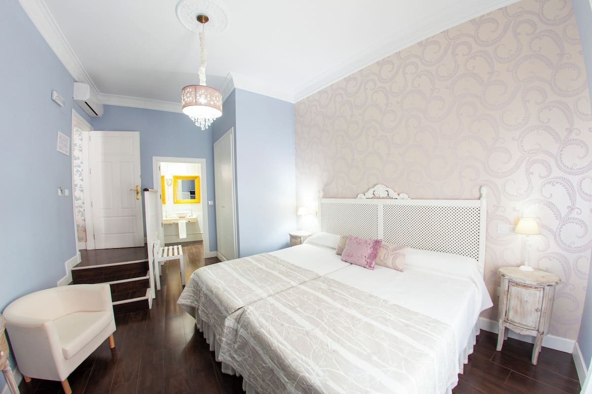 Quarto com uma cama grande, uma cadeira, uma mesa de cabeceira e uma escada que leva a outro cômodo.