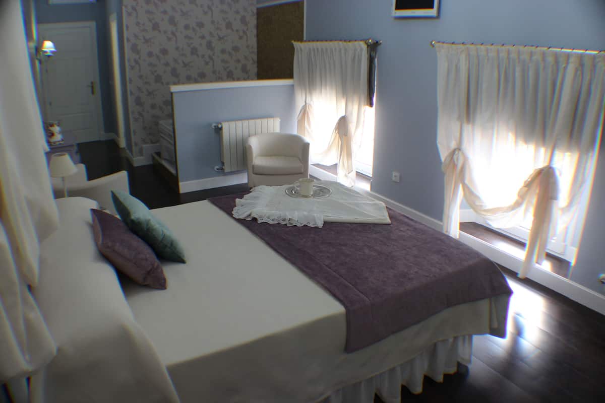 Quarto com cama, cadeira, radiador e cortinas.