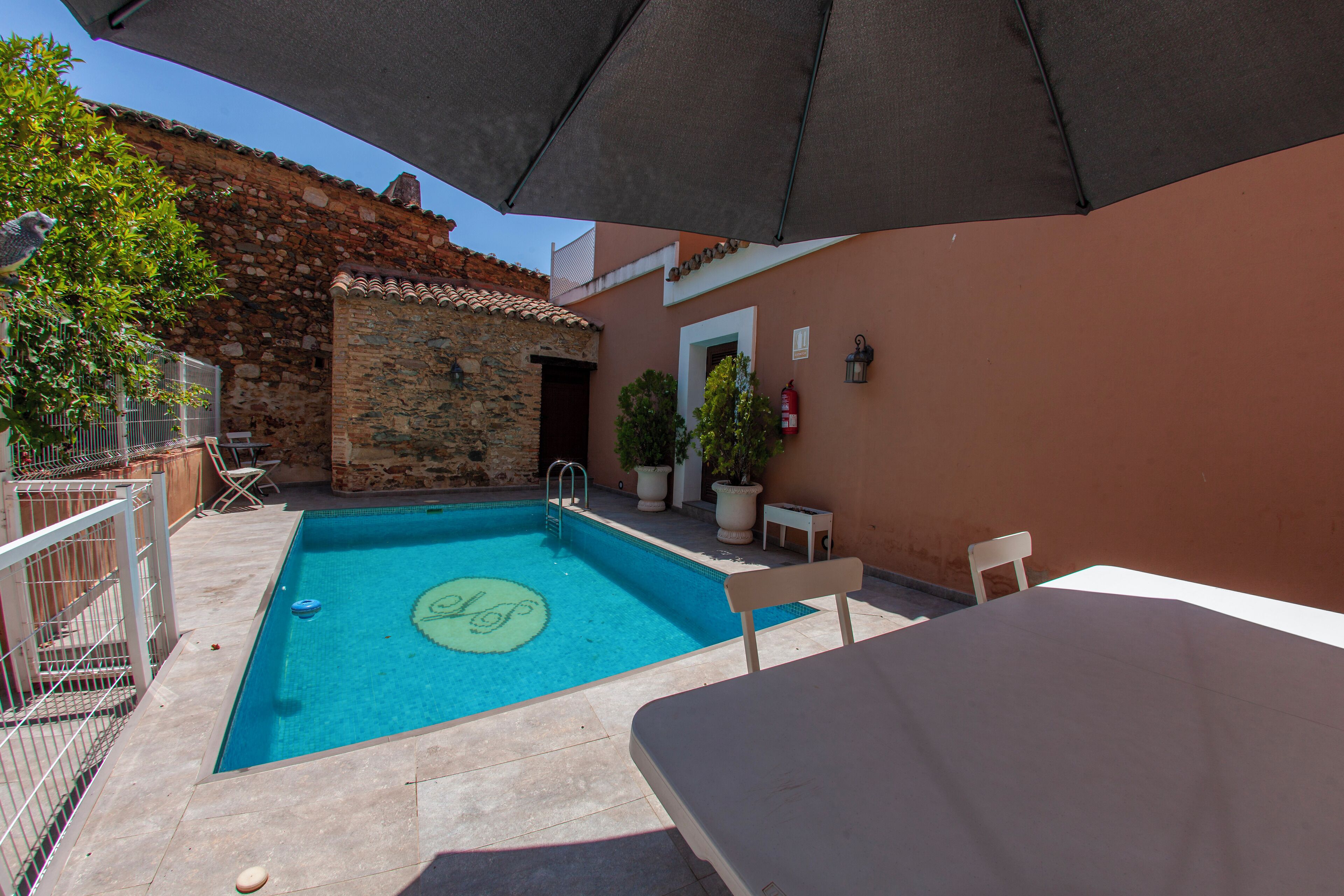 A swimming pool with a stone wall and a door, surrounded by potted plants and outdoor furniture.