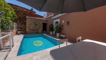A swimming pool with a stone wall and a door, surrounded by potted plants and outdoor furniture.