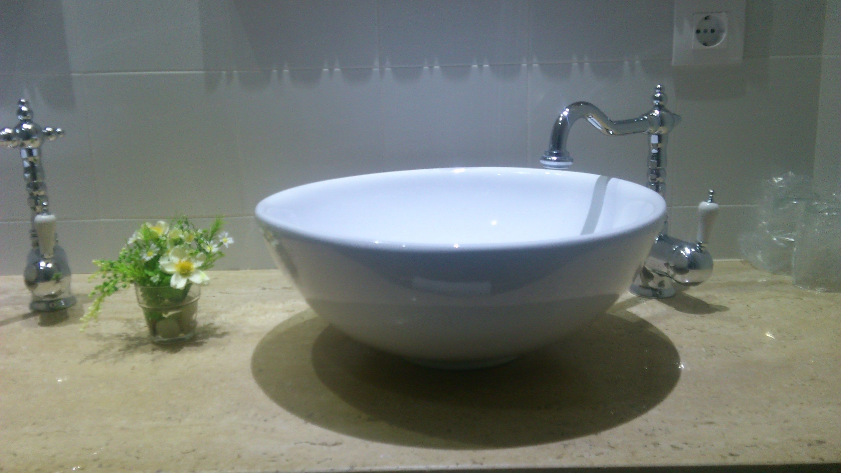 A bathroom sink with a single flower vase and a soap dispenser.