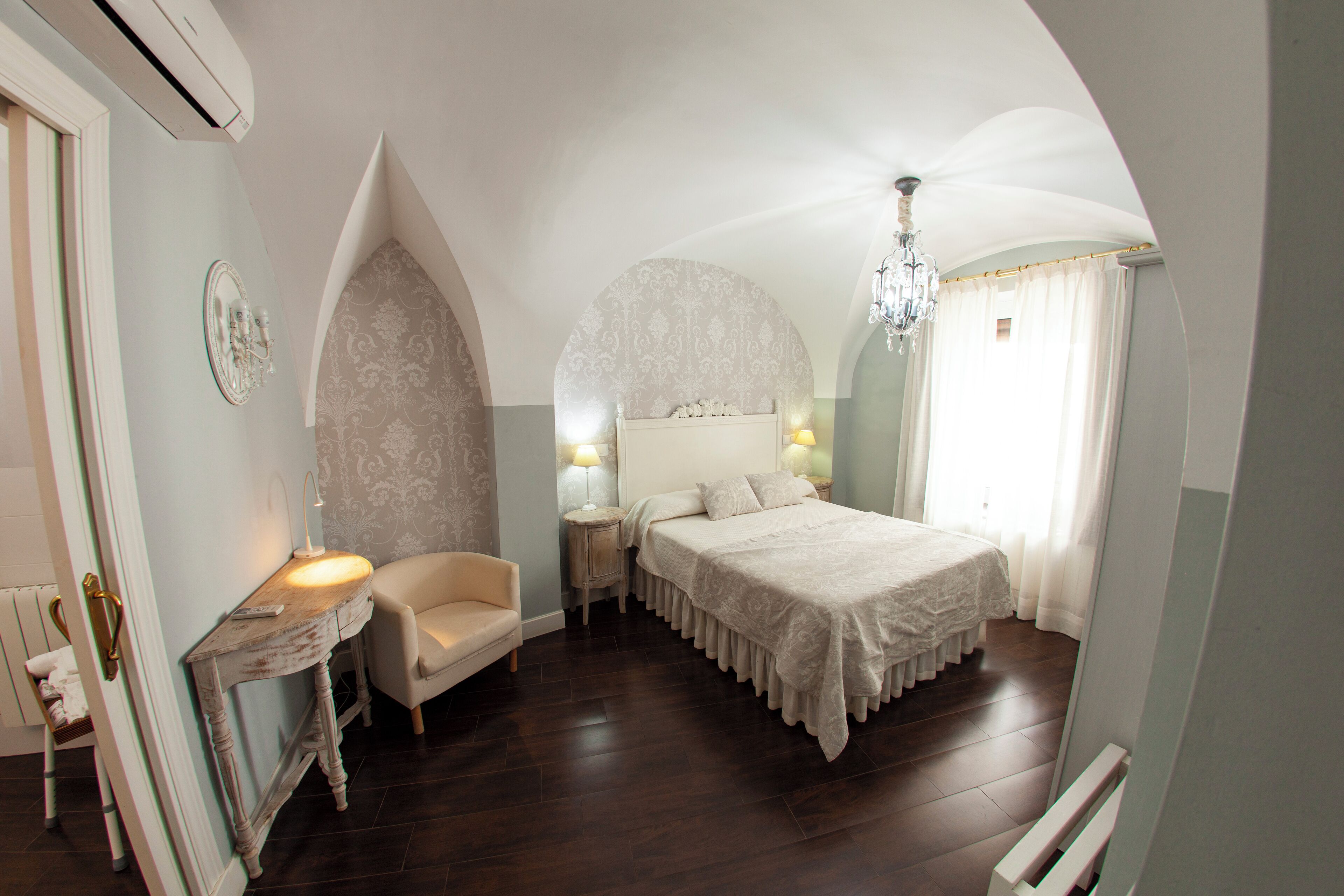 A bedroom with a large bed, a nightstand, a chair, and a vanity with a mirror.