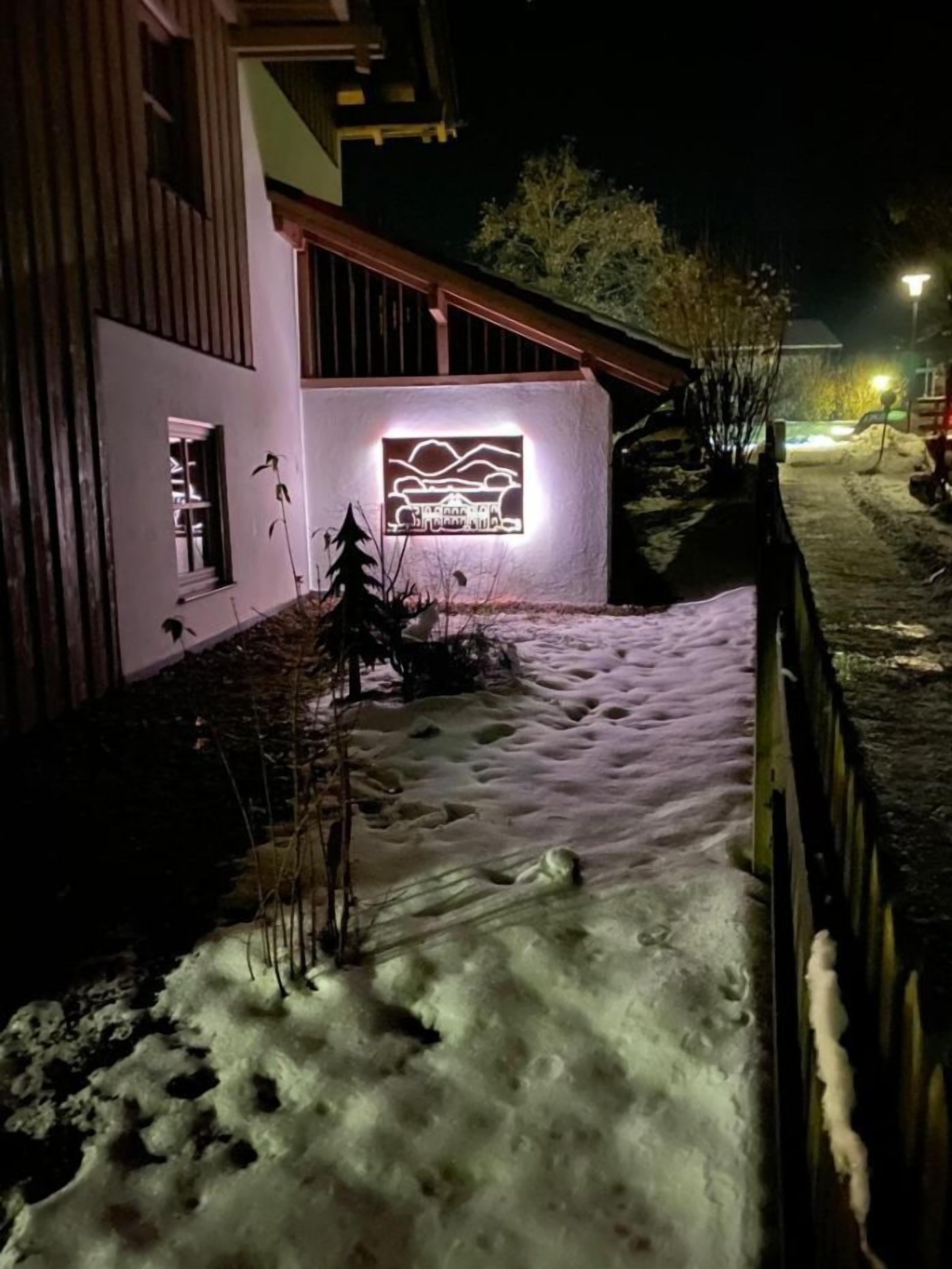 A snow-covered pathway leading to a building with a lit signboard.