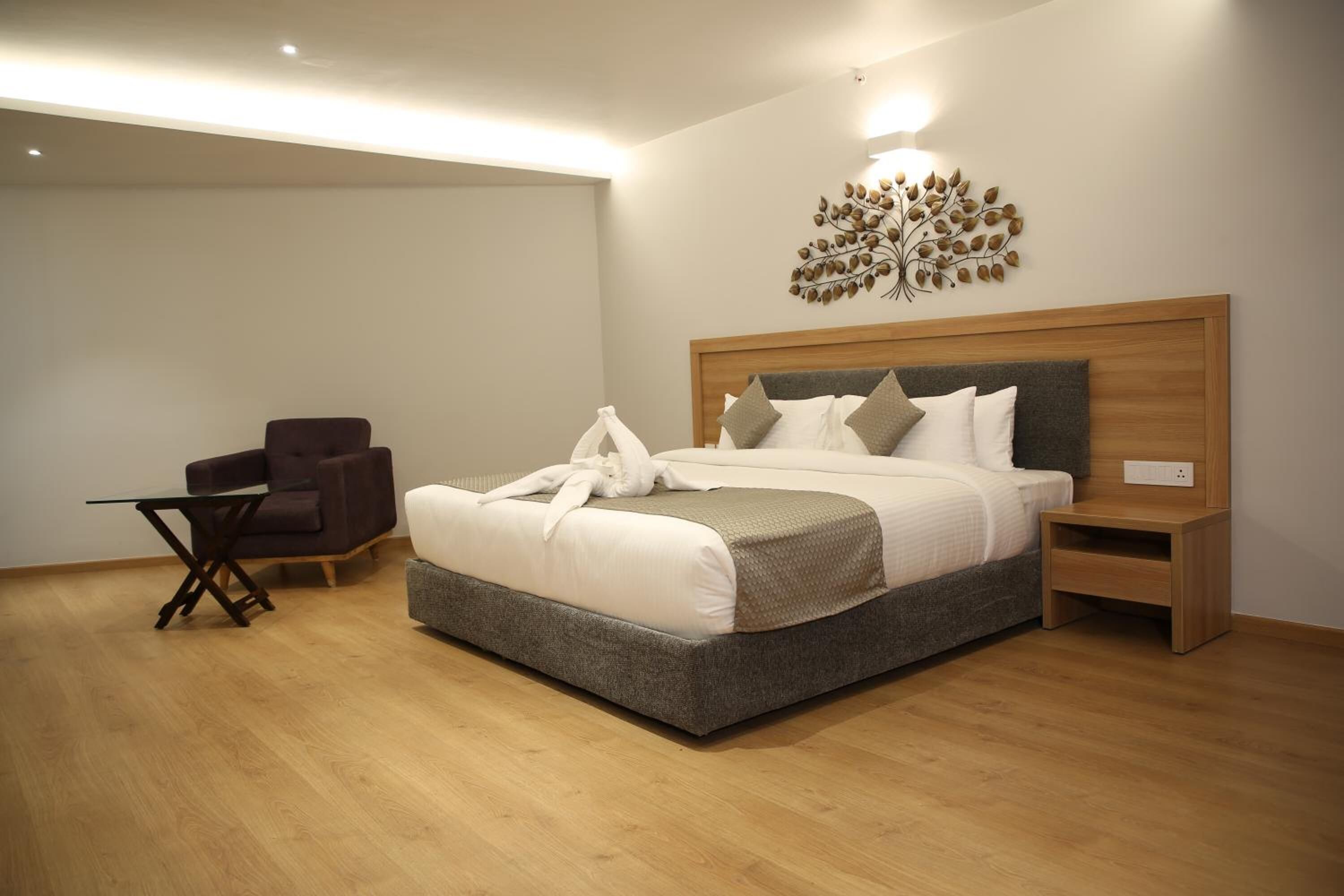 A modern bedroom with a large bed, a chair, a small table, and a decorative wall piece.