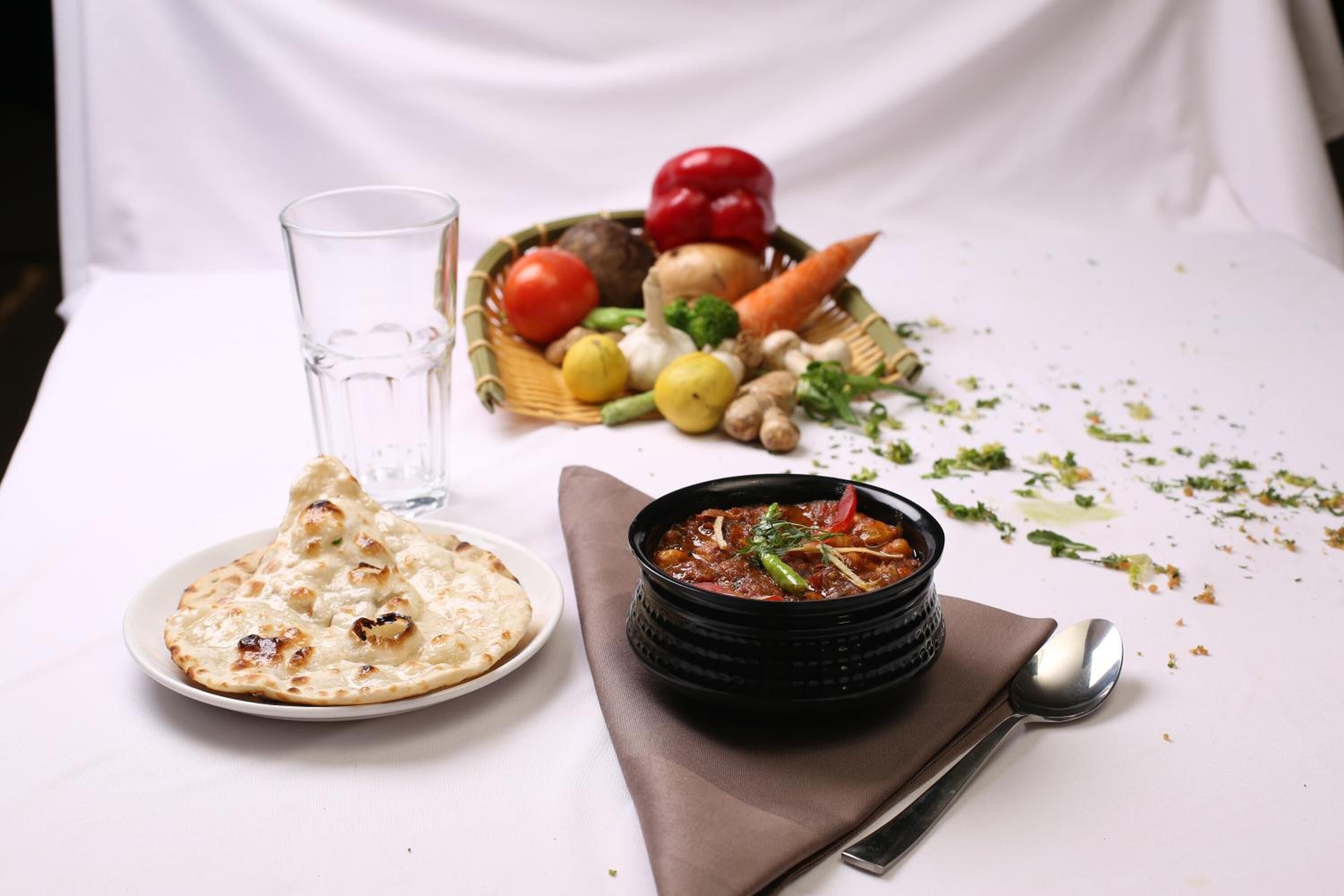 Una mesa con pan naan, un bol de curry y una cesta de verduras frescas.