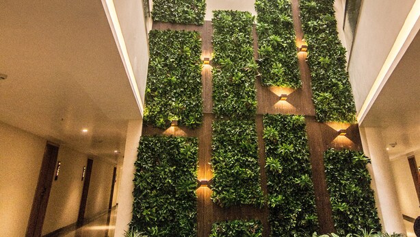 A modern lobby with a central staircase, green vertical gardens, and a geometric ceiling design. - Native By Chancery Hotels (Belagavi)