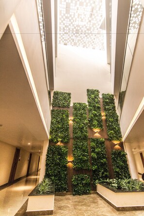 Un vestíbulo moderno con una escalera central, jardines verticales verdes y un diseño geométrico en el techo.
