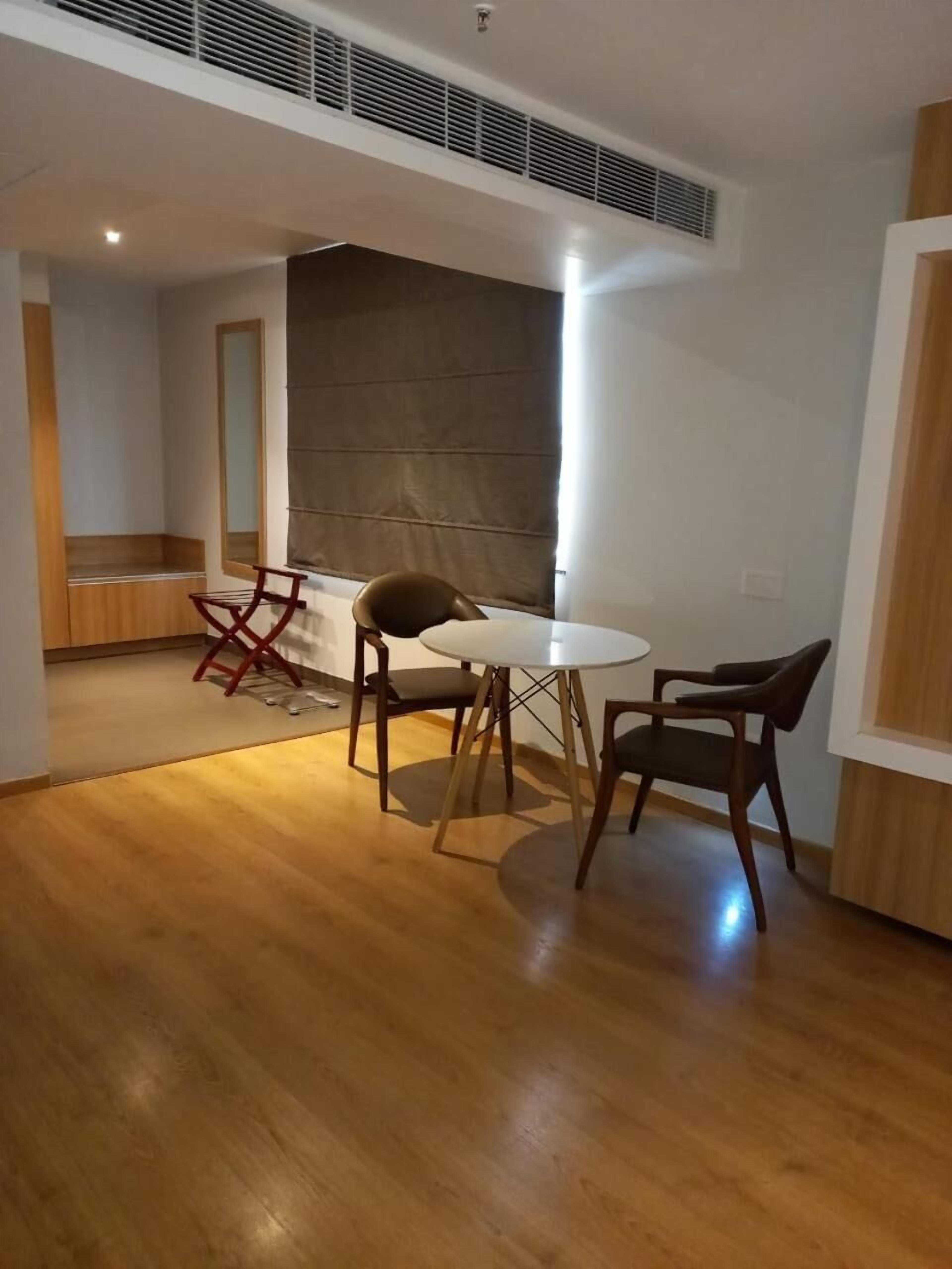 A modern dining area with a round table and four chairs, a wooden floor, and a large window with blinds.