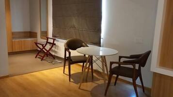 A modern dining area with a round table and four chairs, a wooden floor, and a large window with blinds.