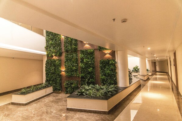 A modern hotel lobby with a long corridor, green vertical gardens, and a marble floor.