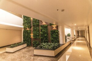 Un lobby de hotel moderno con un largo pasillo, jardines verticales verdes y un suelo de mármol.