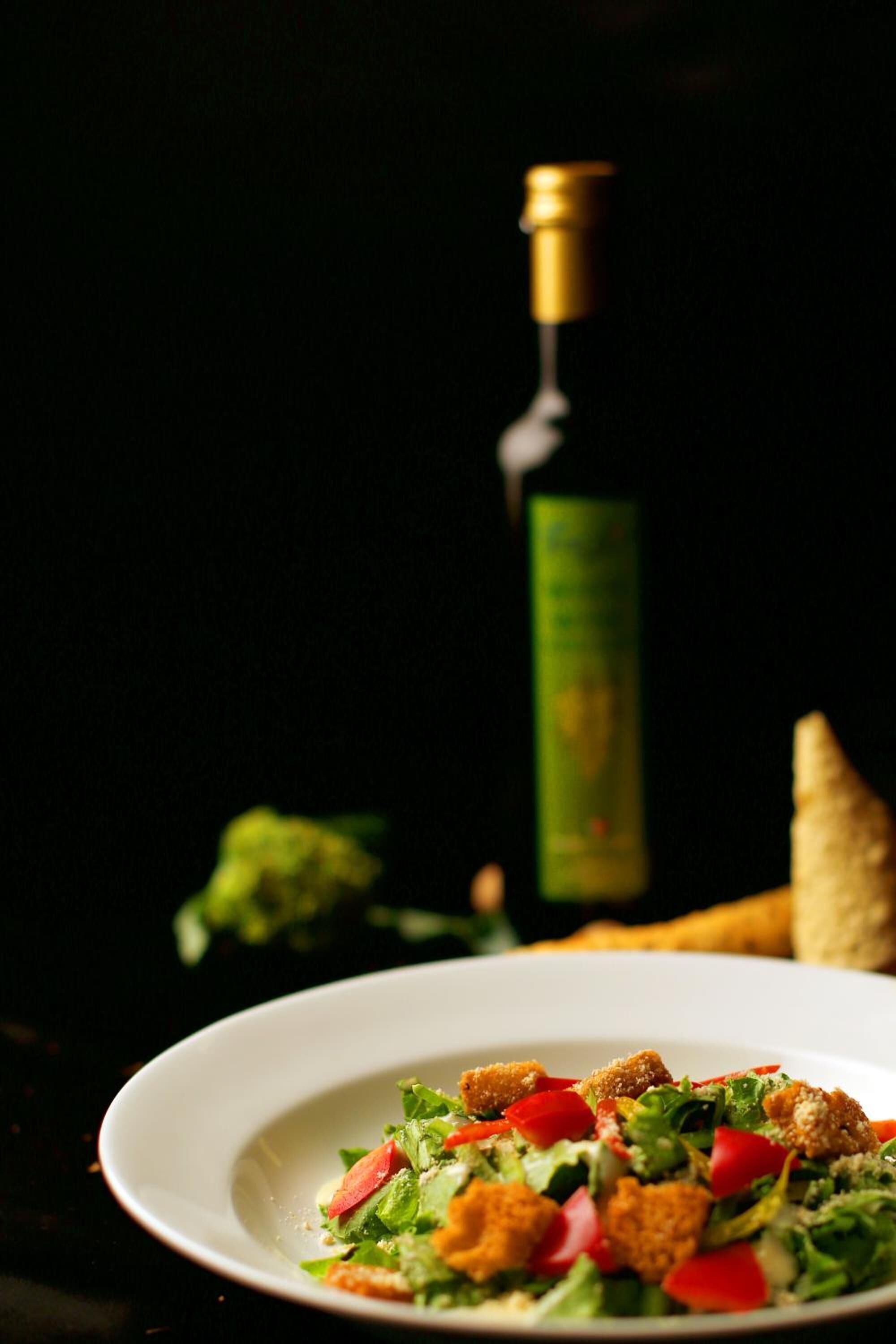 Een salade met croutons en een fles wijn op de achtergrond.