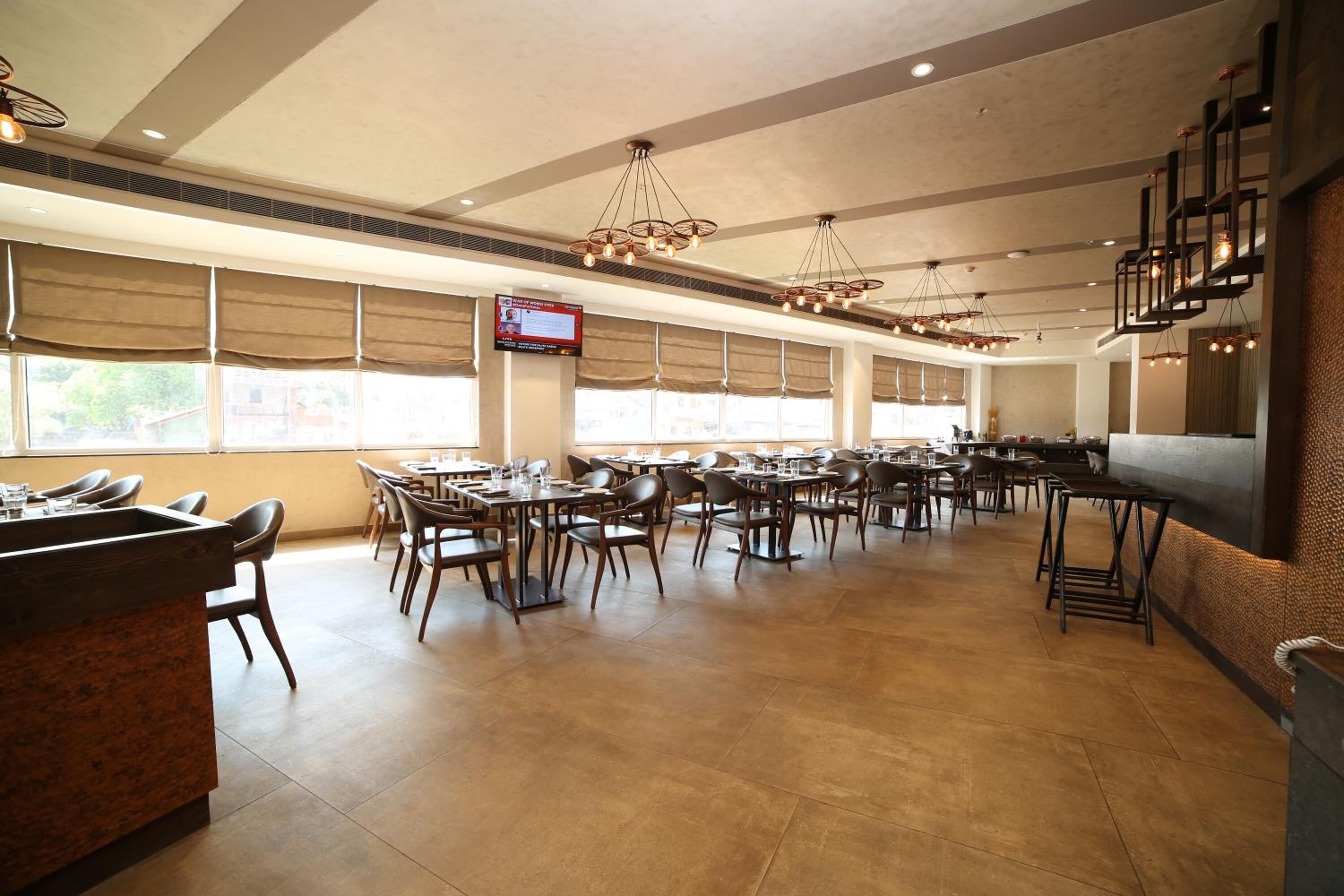 A spacious restaurant with multiple dining tables and chairs, a bar area, and large windows allowing natural light.