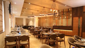 A restaurant with multiple tables and chairs, a counter, and hanging light fixtures. - Native By Chancery Hotels (Belagavi)