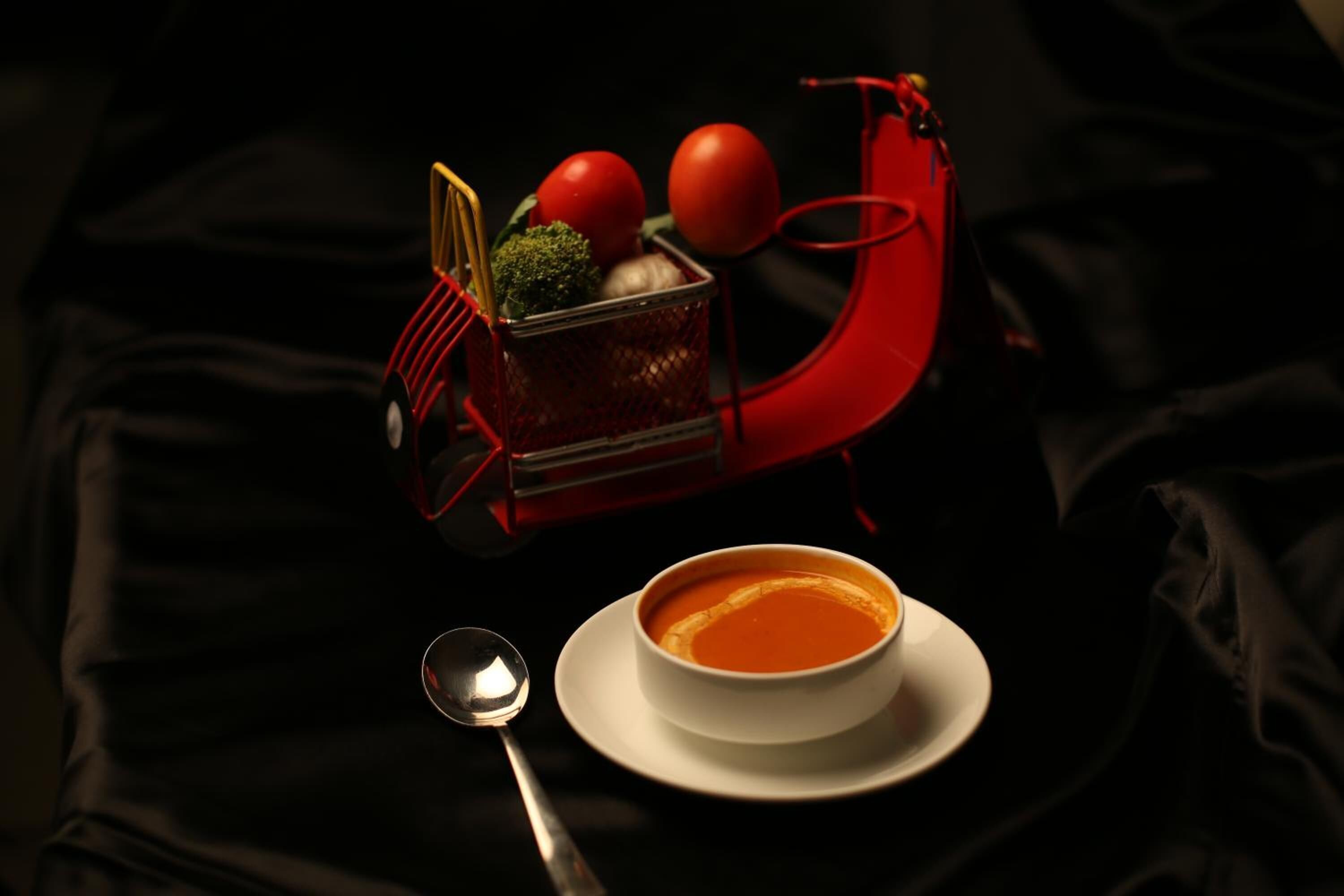 A bowl of soup on a white plate with a spoon beside it, placed on a black cloth.
