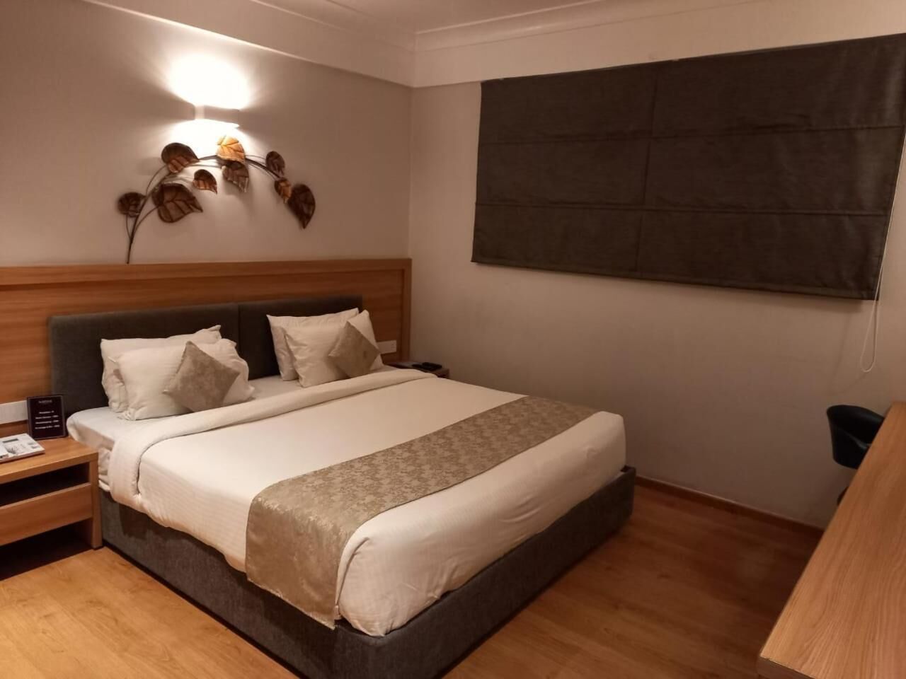 Een hotelkamer met een groot bed, een houten hoofdbord, nachtkastjes en een wandlamp.