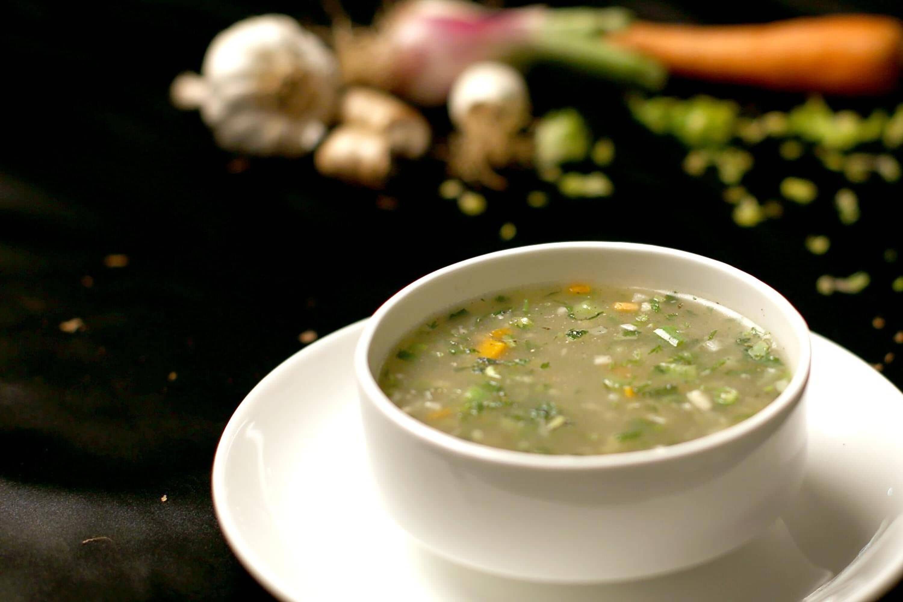 Eine Schüssel Suppe auf einem weißen Teller vor dunklem Hintergrund.