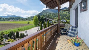 Ein Balkon mit Holzgeländer, einem Tisch mit blauer Tischdecke und einem Blumentopf mit Blumen.