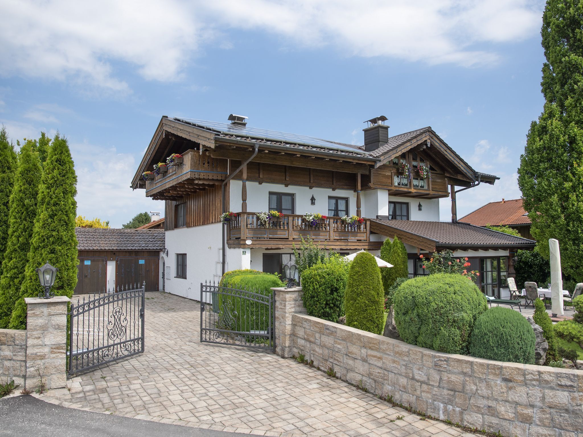 Un chalet à deux étages doté d’un balcon, d’un portail d’entrée en pierre et d’un jardin bien entretenu.