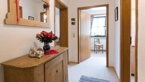 Ein Korridor mit einem Holzschrank, einem Blumenstrauß in einer Vase, einem Spiegel und einer Tür zu einem anderen Raum.