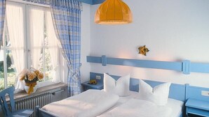A bedroom with a bed, a chair, a nightstand, a window with curtains, and a hanging light fixture.