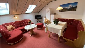 A cozy living room with a red sofa set, a small round table, a television, and a painting on the wall. - Apartment type B 12, 39sqm, balcony, kitchenette, 1 bedroom, 1 living room, WLAN (Ruhpolding)