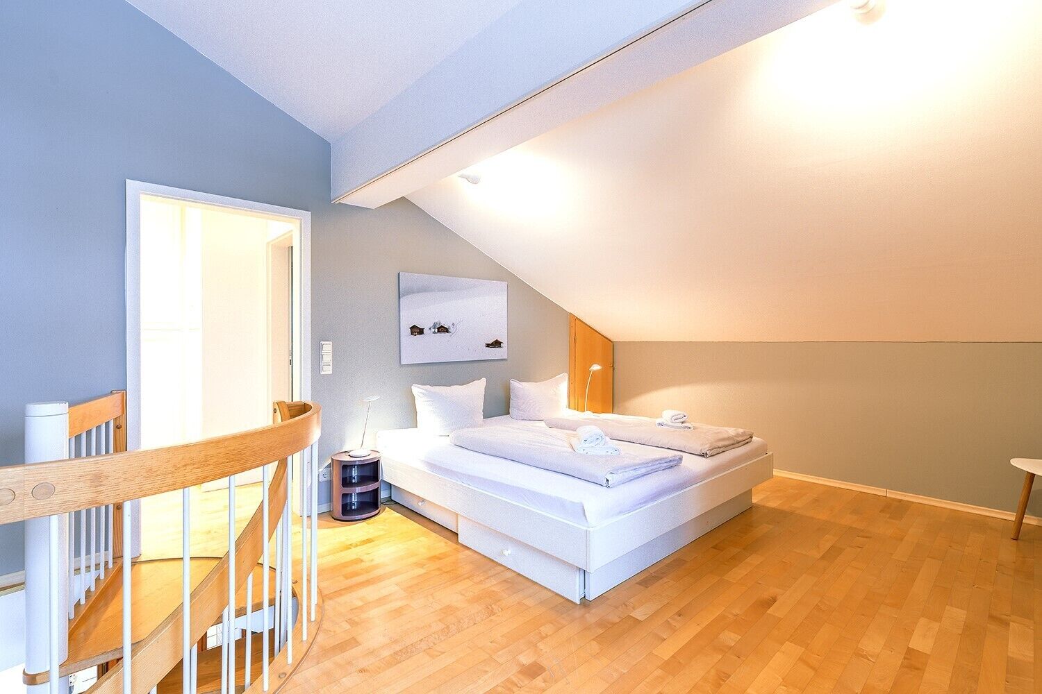 Un dormitorio con una cama grande, una silla de madera, una mesita de noche y una lámpara fijada a la pared.