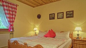 Ein hölzernes Bett mit weißer und rosa Bettdecke, zwei Nachttischlampen und ein Fenster mit karierter Gardine.