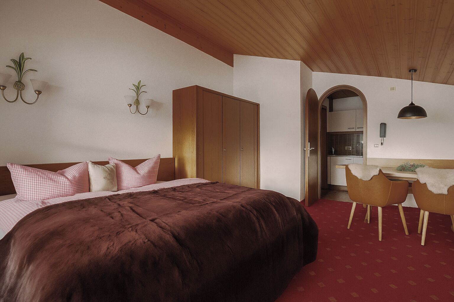 A bedroom with a large bed, wooden wardrobe, and a small dining area with chairs.
