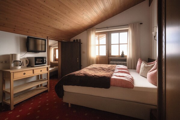 Ein Schlafzimmer mit einem Bett, einem Schreibtisch mit Fernseher, einer Kaffeemaschine und einem Fenster mit Vorhängen.
