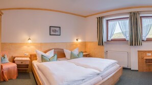 Habitación de hotel con dos camas, un escritorio pequeño, una silla y un ventanal con cortinas.