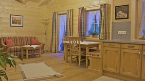 Un accogliente interno di una baita con un tavolo da pranzo in legno, sedie, un divano e un angolo cottura con pensili e un piano di lavoro.