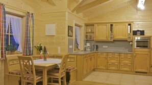 Un interno in legno con un tavolo e sedie da pranzo, una cucina con pensili e elettrodomestici in legno, e una finestra con tende.