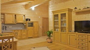 Ambiente interno in legno con cucina, zona pranzo e televisore.