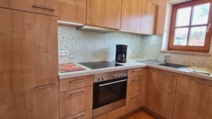 Een kleine keuken met houten kastjes, een inbouwoven, een koffiezetapparaat en een raam met uitzicht.