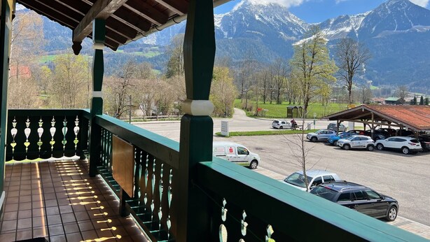 Een overdekt balkon met uitzicht op een bergketen en een parkeerplaats met auto's.