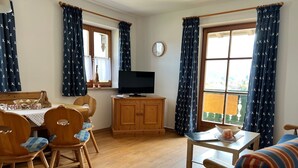 Een gezellige woonkamer met een houten eettafel, stoelen, een televisie en een bank.