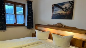 Een tweepersoonsbed met twee kussens, een houten hoofdbord, een nachtkastje en een raam met gordijnen.
