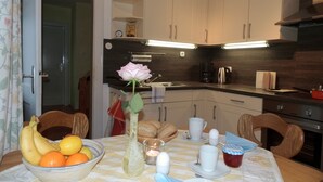 Een moderne keuken met houten kastjes, een eettafel gedekt met fruit, een vaas met een bloem en een koffiezetapparaat.