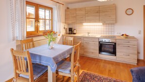 A kitchen with wooden cabinets, a built-in oven, and a dining area with a table and chairs. - Apartment 2, 55sqm, balcony, kitchenette, 2 bedrooms, 1 living room, WLAN (Ruhpolding)